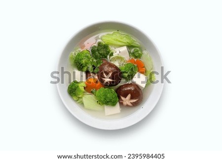 Bowl of clear soup with mix veggy vegetables carrot, brocolli, black shiitake mushrooms tofu. View from top vegetarian vietnamese mushroom clear soup bowl on white background