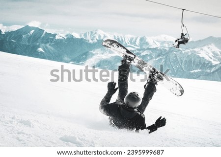 Snowboarder fall down on back painfully with snow splashes on snowy off-piste ski slope and old chair lift at background. Sunny winter day. Black and white toned image. Royalty-Free Stock Photo #2395999687