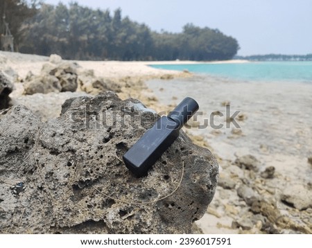 Mock up of Black Small Perfume Bottle by the Rocky Tropical Beach, with distant sky and trees in the background
