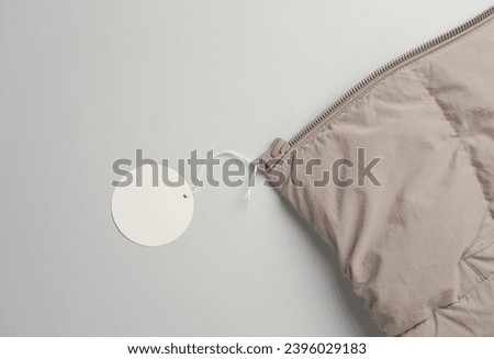 Winter down jacket with white blank tag on a string. Shopping, sale concept. Template for design Royalty-Free Stock Photo #2396029183