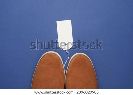 Suede shoes with white blank tag on string, blue background. Template for design, sale, shopping concept