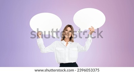 Portrait of cheerful young European businesswoman holding two blank speech bubbles standing over purple background. Concept of communication Royalty-Free Stock Photo #2396053375