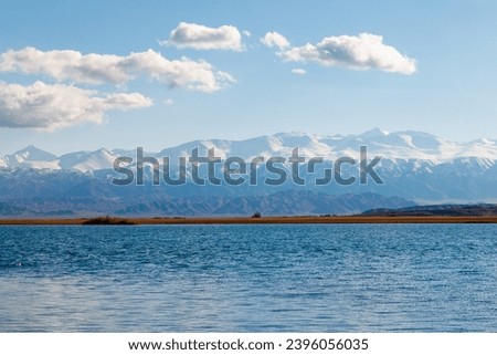 Blue calm water in Issyk-Kul lake with mountains on background at summer day.