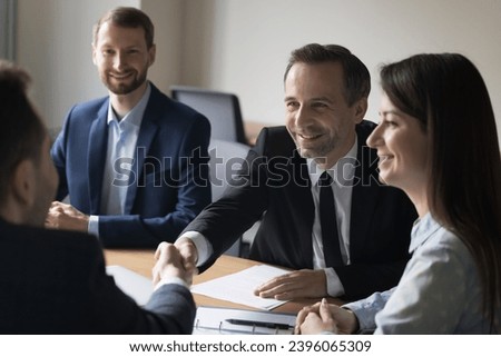 Happy businessman shake hand of new business partner, celebrate conclusion of great deal, reach agreement, sign contract, smiling team leader welcomes colleague at team brainstorming meeting at office