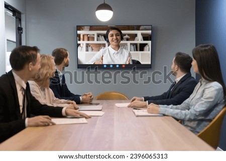 Indian woman leads on-line conference with diverse teammates sit at desk look at tv screen sit at desk in modern boardroom. HR manager interviewing Indian woman applicant answer questions at interview Royalty-Free Stock Photo #2396065313