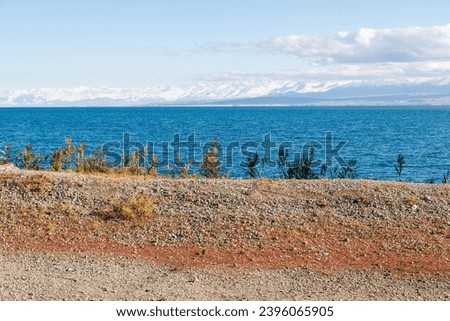 Blue calm water in Issyk-Kul lake with mountains at the background and grass shore in the foreground at summer day.