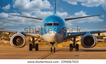 front view of blue and silver commercial airliner taxiing on runway on a beautiful cotton cloud day Royalty-Free Stock Photo #2396067425