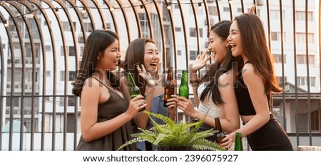 Group of happy Asian girl friends celebrating party with beer bottle toasting drinks at rooftop bar restaurant in sunset together, woman chatting, laughing, night lifestyle