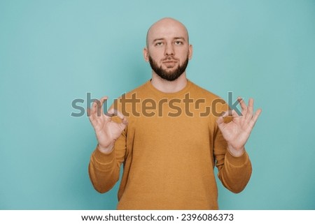 calm bald bearded man in casual holds hands in meditative gesture against turquoise background. focus concept. Mental balance concept. Keep calm.