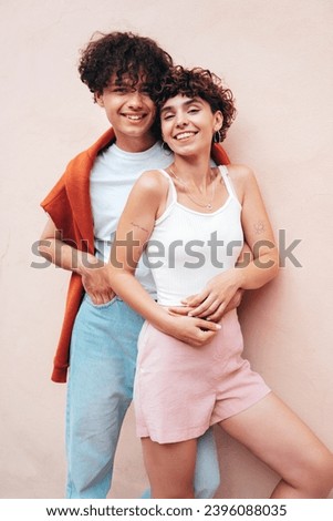 Young smiling beautiful woman and her handsome boyfriend in casual summer clothes. Happy cheerful family. Female having fun. Couple posing in street at sunny day. Near  wall. Having tender moments