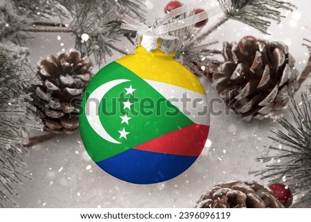 Christmas ball with the flag of Comoros, decorates the snow tree with snowfall. The concept of the Christmas and New Year holiday