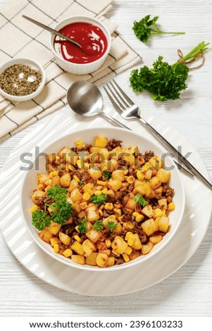 Cowboy Beef Hash with roasted corn, garlic and parsley in white bowl on wooden table with spoon and fork, vertical view from above