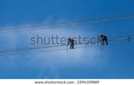 Electrician in protective helmet working on high voltage power lines. Highly skilled workmen servicing the electricity grid, Technician works in a bucket high up on a power pole. Royalty-Free Stock Photo #2396109889