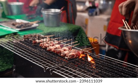 Picture of grilled food which is being placed on the barbecue grill Flames spread across the barbecue. At a flea market The seller is about to use her hands to turn the stick upside down. 