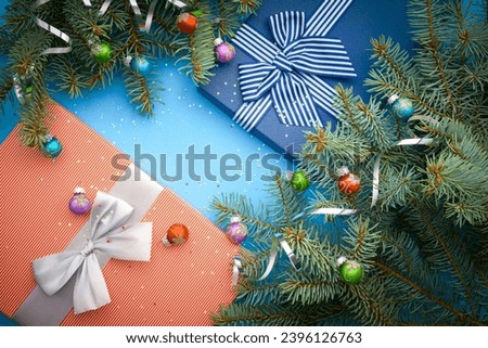 Red striped gift box with a silver bow and blue gift box with blue stripted ribbon.   Holidays card with gift boxes, branch, little stars and balls. Gigt boxes lie on a blue textured background
