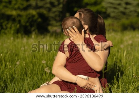 A tender embrace in a field, a mother and child in matching outfits share a moment of closeness. The warm sunlight enhances the feeling of maternal love.