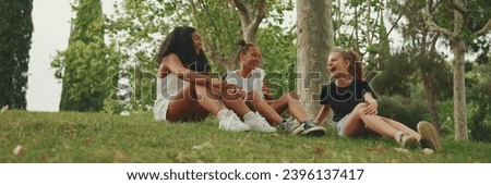 Three girls friends pre-teenage sit on the grass in the park and emotionally talking. Three teenagers on the outdoors Royalty-Free Stock Photo #2396137417