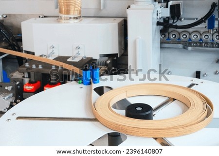 Machine tools for gluing edging onto furniture wood board, Edging PVC. Photo of cutter machine, close-up, coil with melamine edge Royalty-Free Stock Photo #2396140807