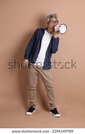 Asian man holding a megaphone on isolated brown background