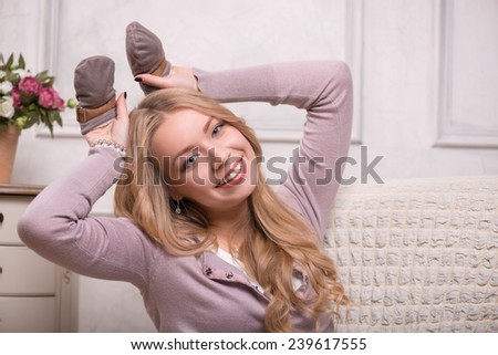 Closeup portrait of young attractive happy Caucasian woman sitting in armchair holding baby mittens and putting them by her head like rabbit ears, interior shot, baby expectation concept