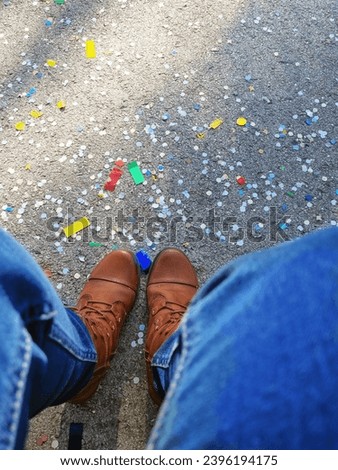 after the festival, confetti on the asphalt underfoot, view down, boots and jeans, holiday, fiesta, high day, gala day, playday, red-letter day Royalty-Free Stock Photo #2396194175