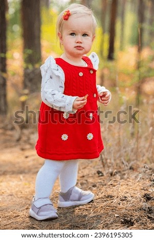 The sweetest child toddler girl in a red dress in the autumn forest. Happy childrens day. Active outdoor games, fun and happy concept of carefree childhood