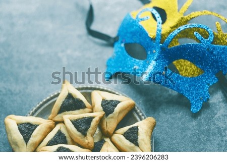 Traditional Hamantash triangular cookie with poppy seed filling, carnival masks on a concrete background. space for text. Purim celebration concept. Jewish carnival holiday. High quality photo