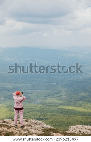 Female tourist taking pictures of the landscape from the top of the mountain while hiking