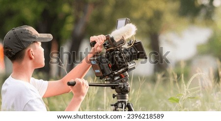 Teenage boy operating film camera in the movie industry. new content creator, young filmmaker. Royalty-Free Stock Photo #2396218589