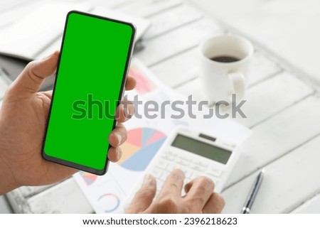 Businessmen use an empty smartphone at the coffee shop. His Hands are holding the smartphone with a green screen. and another hand are pressing the calculator. Financial development, Banking Account, 