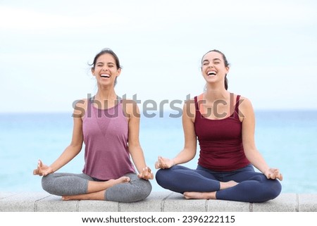 Two happy yogis laughing doing yoga on the beach Royalty-Free Stock Photo #2396222115