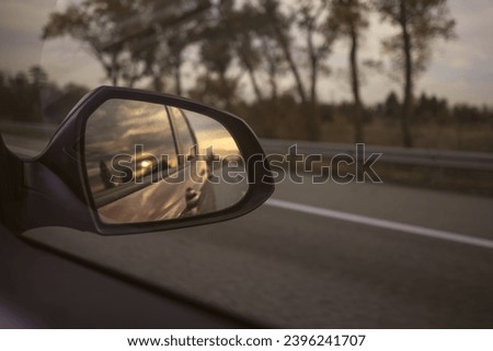 The reflection of the sunset sky in the car's side view mirror. Car trip. View through the car window. The romance of the road.