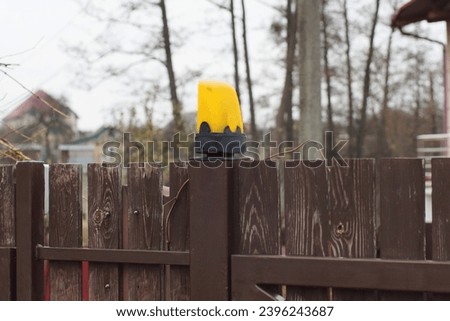 one yellow black large glass yellow signal light stands on a brown wooden fence wall on the street