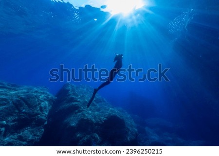Underwater backlit photo of a woman diving into the Mediterranean
