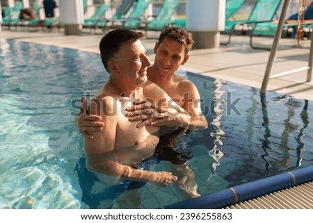Rehab therapy session in a pool with a trainer assisting a happy patient. Aqua fitness concept image. Royalty-Free Stock Photo #2396255863