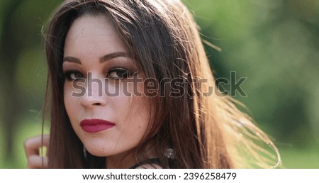 Millennial young woman posing to camera in outdoor park. Pretty hispanic girl headshot