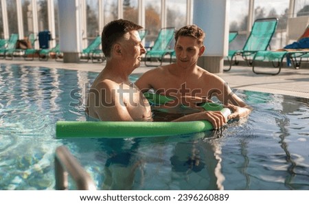 Two men engaged in conversation during aquatic rehab with pool noodles Royalty-Free Stock Photo #2396260889