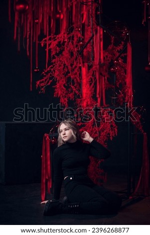 A beautiful young blonde girl in New Year's red clothes in an atmospheric photo studio with a stylish festive interior in red colors.