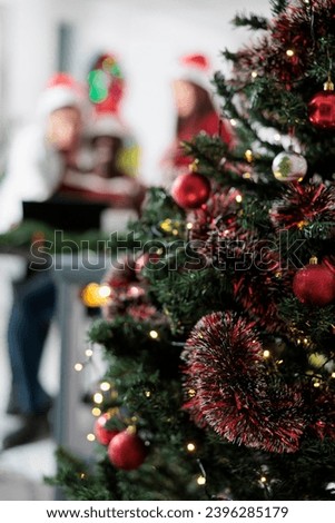 Close up focus shot on office xmas tree in festive decorated workspace with business coworkers working in the background. Christmas ornate company workplace during winter holiday season