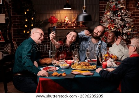 Family taking photos at christmas dinner with delicious food and glasses of wine, making memories during december holiday event. Diverse people having fun with pictures on smartphone at home.