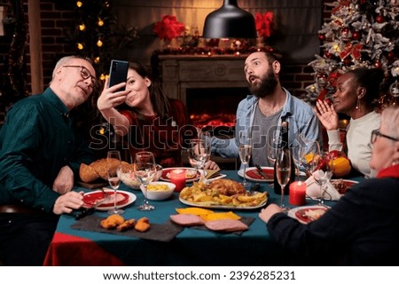 People taking pictures at festive dinner with homemade food and glasses of wine, making memories during christmas eve winter holiday. Diverse persons having fun with photos on phone at home.