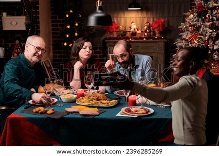 Persons taking photos at festive dinner, making memories of christmas eve celebration at home. Diverse friends and family having fun with drinks and food, taking pictures with smartphone.