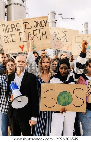 Organized group of diverse people with posters and placards protesting against climate change in the world in front of a polluting factory. Environmental conservation and global warming concept.