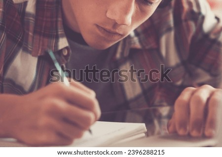 caucasian teenager indoor doing homework on the table at home - blonde guy writing and reading in his laptop or computer to get greats scores - portrait of boy with headphones Royalty-Free Stock Photo #2396288215