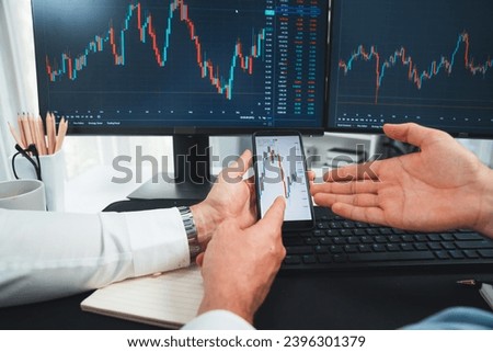 Cropped photo of exchange traders pointing lowest chart stage on dynamic graph with smartphone on hand focus, analyzing comparing with monitor and phone, discussing financial technology. Sellable.