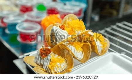Picture of a type of dessert sold at temple fairs This kind of dessert is known in Thai as Khanom Bueng. It has a thin crispy dough sheet supported by a thick and soft cream. Garnish with golden floss