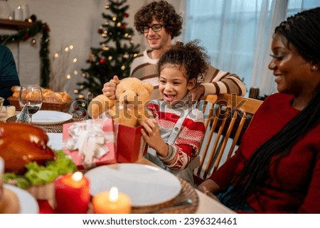 Multi-ethnic family giving gift box to daughter during Christmas party. Attractive little girl receive present from relative while having dinner celebrate holiday Thanksgiving on dining table in house