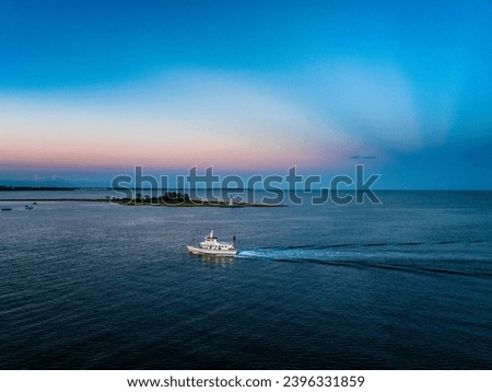 Boat cruising past lighthouse into calm harbor at sunset Black Rock Connecticut Royalty-Free Stock Photo #2396331859