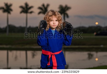 Kid boy practicing martial arts outdoor. Sport martial arts, boxing kids. Little boy wearing kimono doing boxing in park. Child with boxing gloves training martial arts. Little fighter. Boxing for Royalty-Free Stock Photo #2396335829