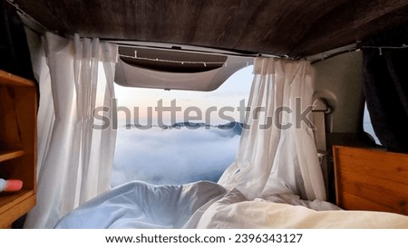 Beautiful cloudy view from bed in camper van with unmade bed, pillow, and white curtain at Watu Mabur Yogyakarta, Indonesia